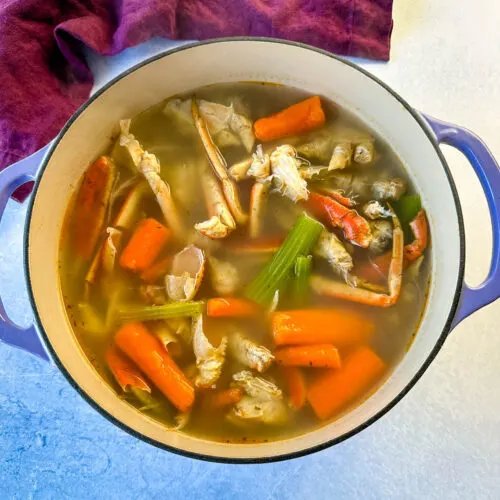 homemade seafood stock with crab shells, carrots, and celery in a Dutch oven