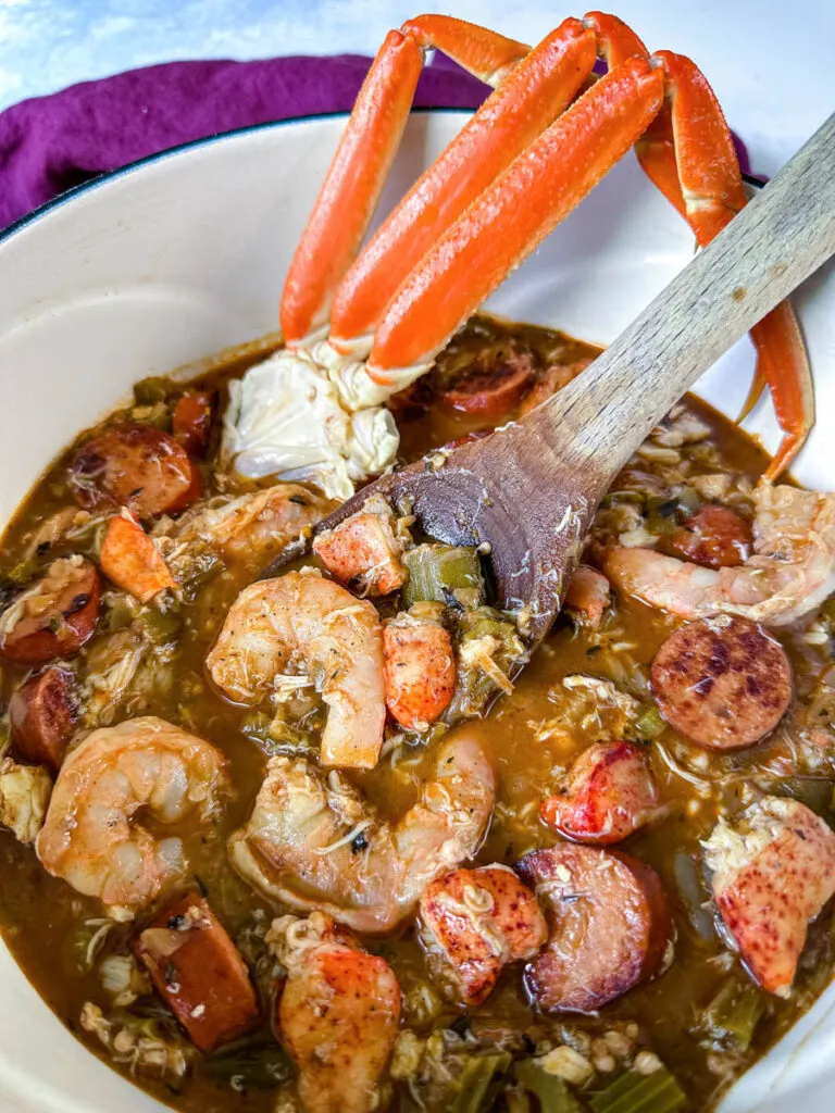 Cajun seafood gumbo with shrimp and crab meat and crab legs with rice in a Dutch oven with a wooden spoon