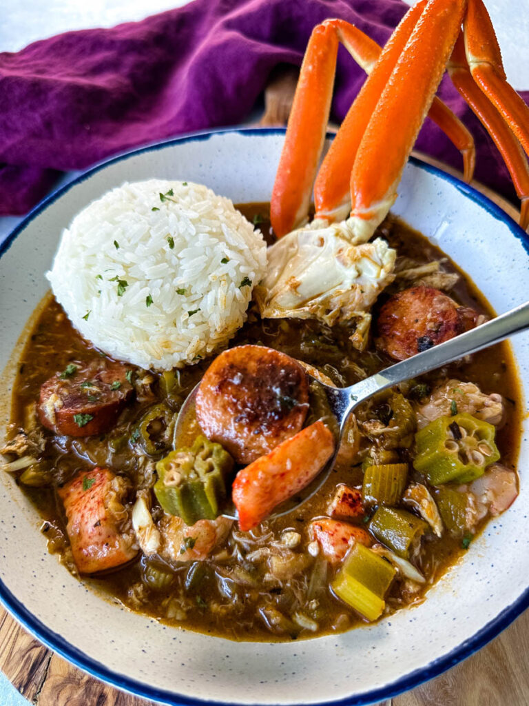 spoonful of Cajun seafood gumbo with shrimp and crab meat and crab legs with rice in a white bowl