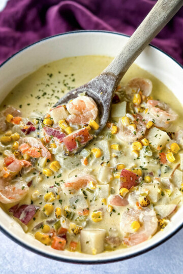 shrimp and corn chowder with bacon and potatoes with a wooden spoon in a Dutch oven