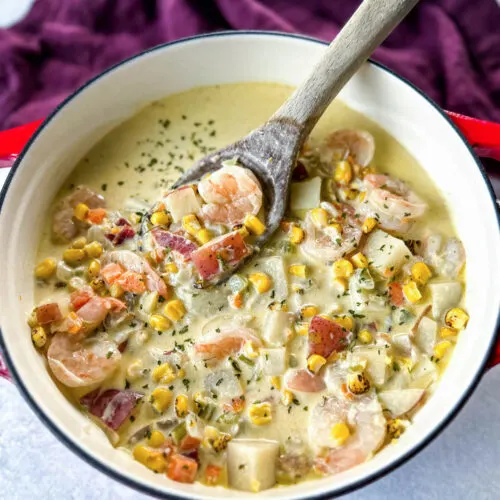 shrimp and corn chowder with bacon and potatoes with a wooden spoon in a Dutch oven