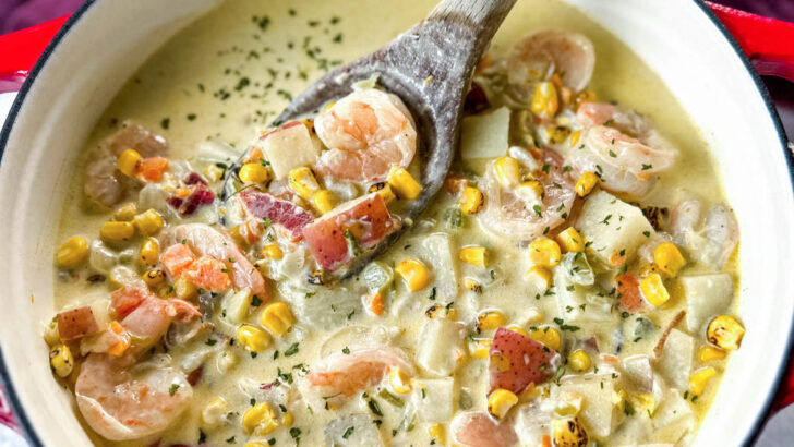 shrimp and corn chowder with bacon and potatoes with a wooden spoon in a Dutch oven