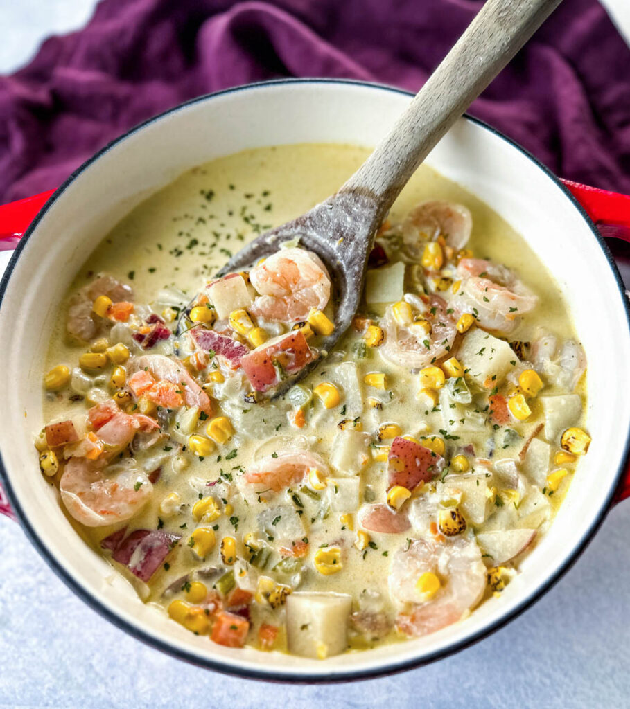 shrimp and corn chowder with bacon and potatoes with a wooden spoon in a Dutch oven