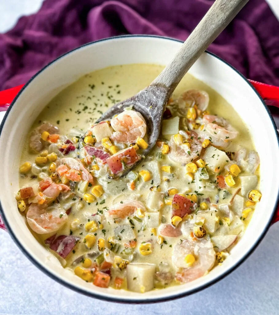 shrimp and corn chowder with bacon and potatoes with a wooden spoon in a Dutch oven