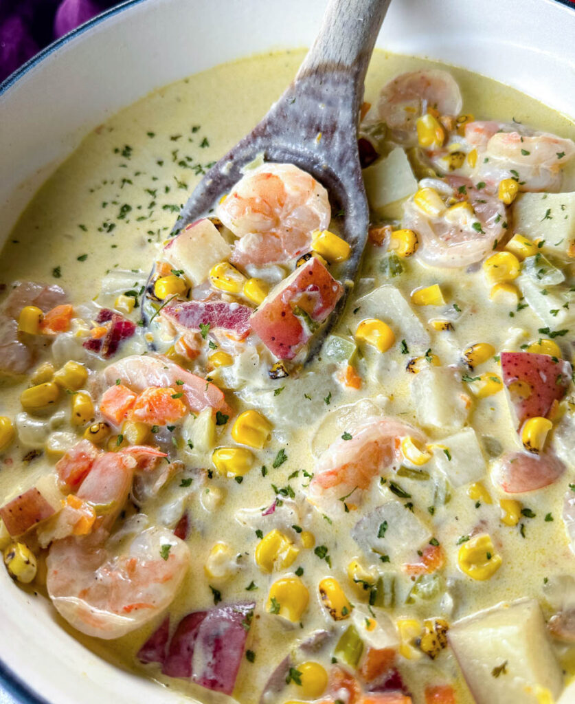 shrimp and corn chowder with bacon and potatoes with a wooden spoon in a Dutch oven