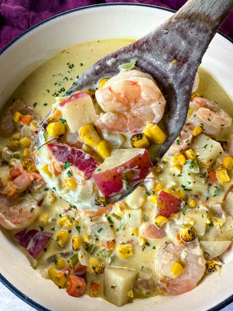 shrimp and corn chowder with bacon and potatoes with a wooden spoon in a Dutch oven