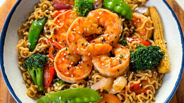 shrimp stir fry with noodles, vegetables, and a homemade sauce in a white bowl