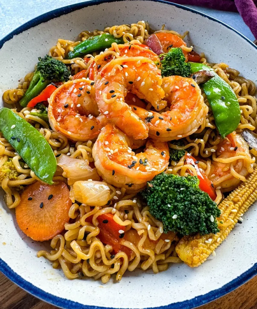 shrimp stir fry with noodles, vegetables, and a homemade sauce in a white bowl