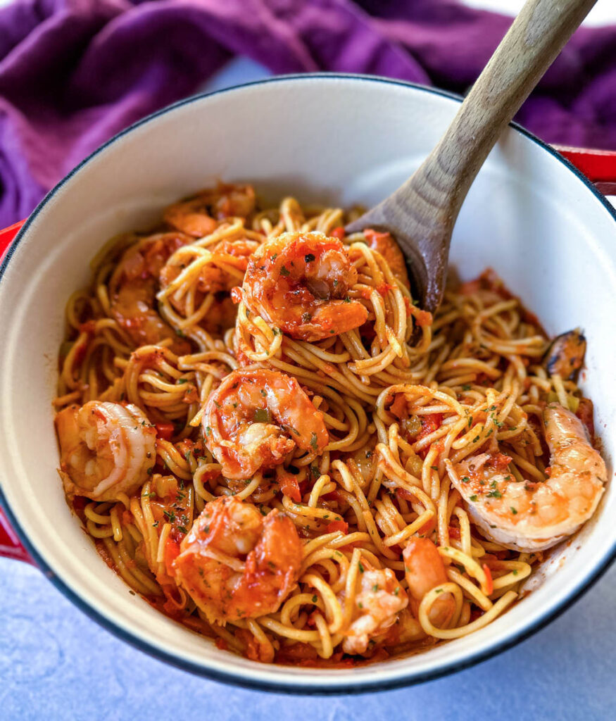 shrimp spaghetti with garlic in a Dutch oven with a wooden spoon