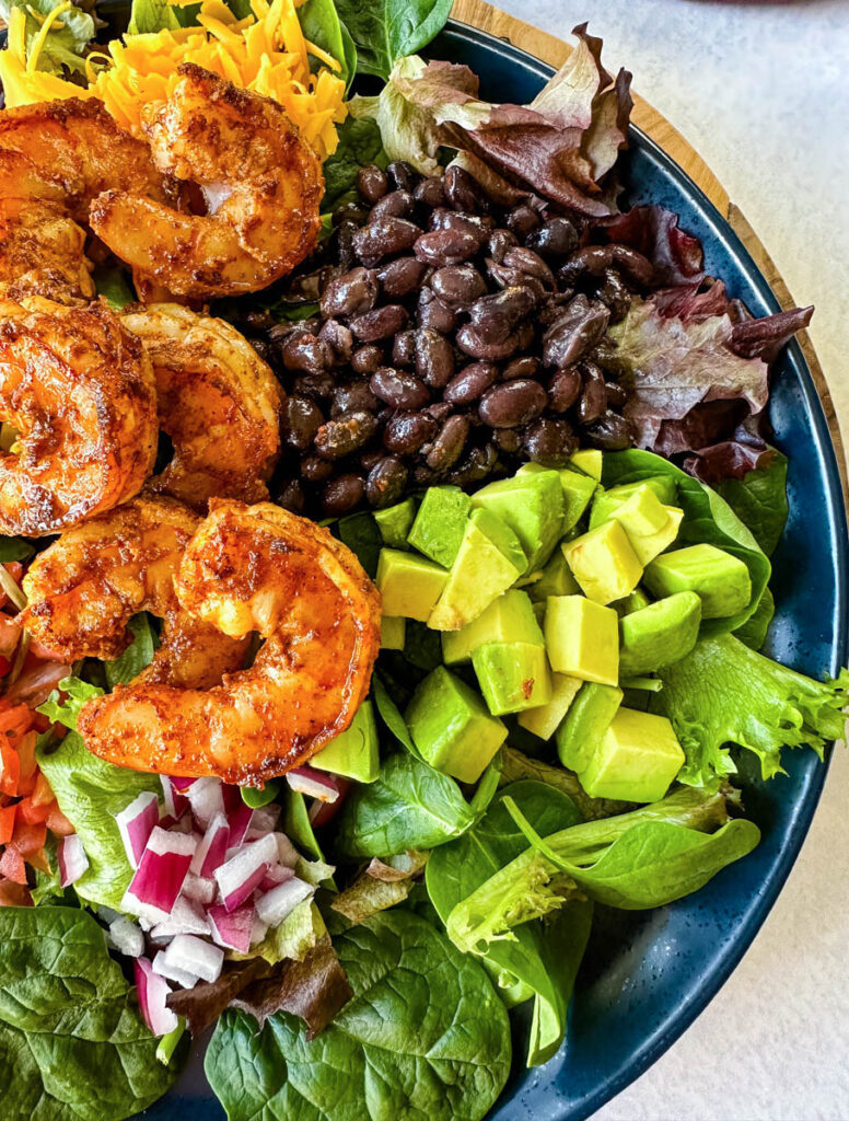 shrimp taco salad with avocado, corn, black beans, onions and salsa on a blue plate