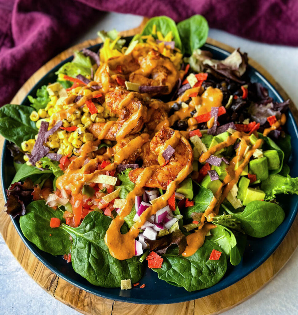 shrimp taco salad with avocado, corn, black beans, onions and salsa on a blue plate with Chipotle ranch dressing