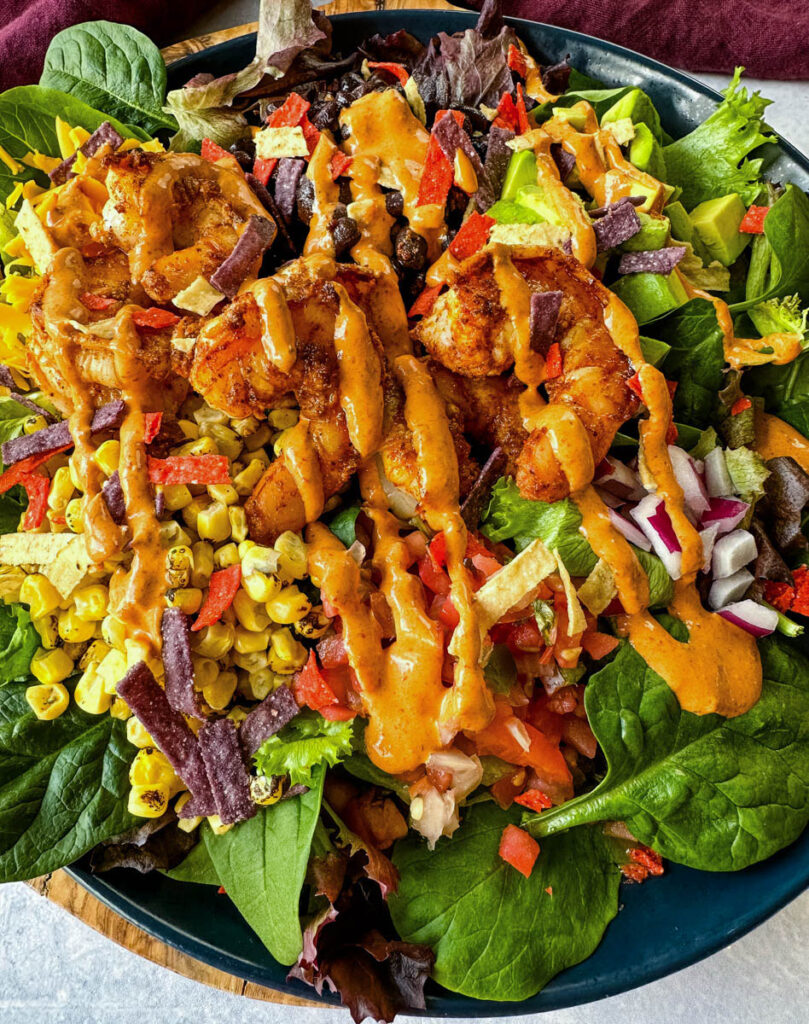 shrimp taco salad with avocado, corn, black beans, onions and salsa on a blue plate with Chipotle ranch dressing