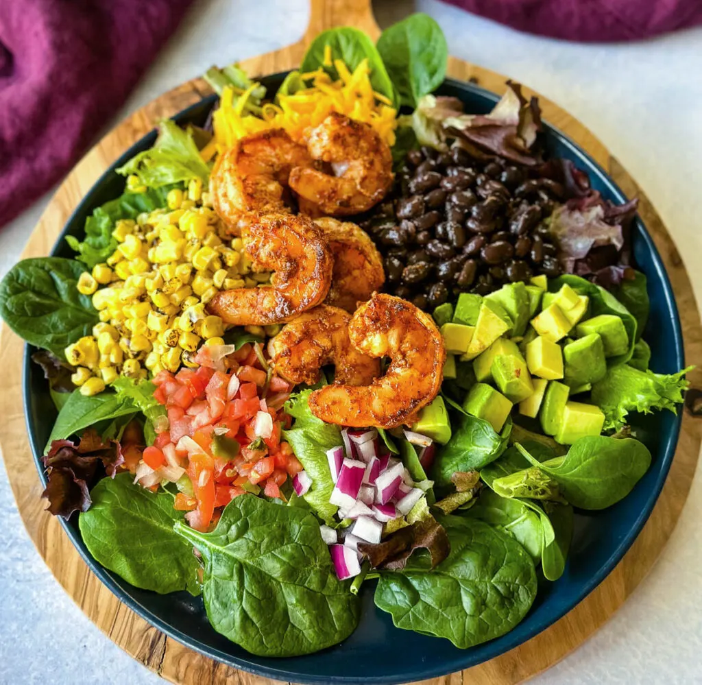 shrimp taco salad with avocado, corn, black beans, onions and salsa on a blue plate