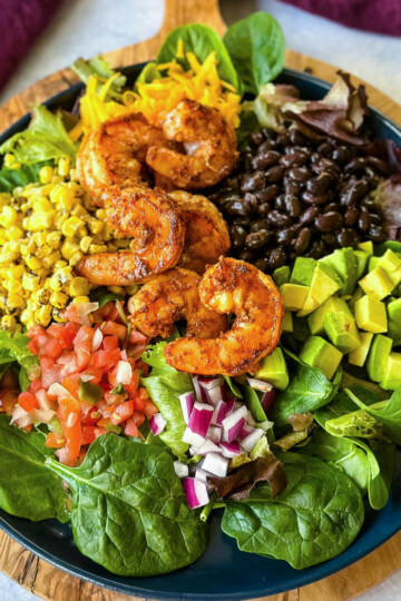 shrimp taco salad with avocado, corn, black beans, onions and salsa on a blue plate