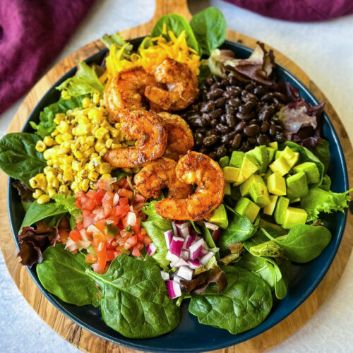 shrimp taco salad with avocado, corn, black beans, onions and salsa on a blue plate