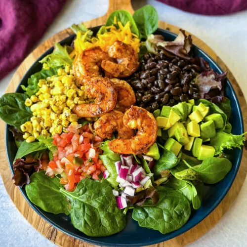 shrimp taco salad with avocado, corn, black beans, onions and salsa on a blue plate