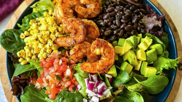 shrimp taco salad with avocado, corn, black beans, onions and salsa on a blue plate