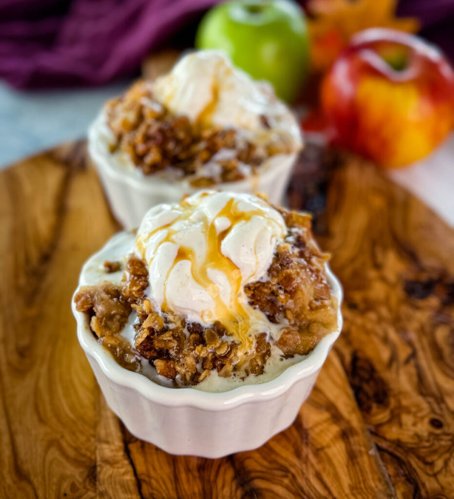 slow cooker Crockpot apple crisp in a white bowl with a scoop of vanilla ice cream and caramel