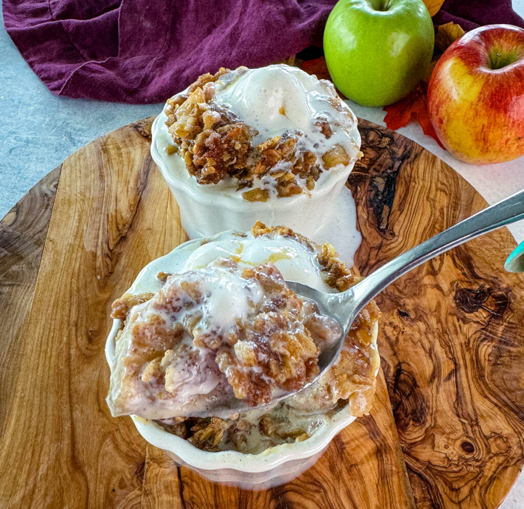 a spoonful of slow cooker Crockpot apple crisp in a white bowl with a scoop of vanilla ice cream and caramel