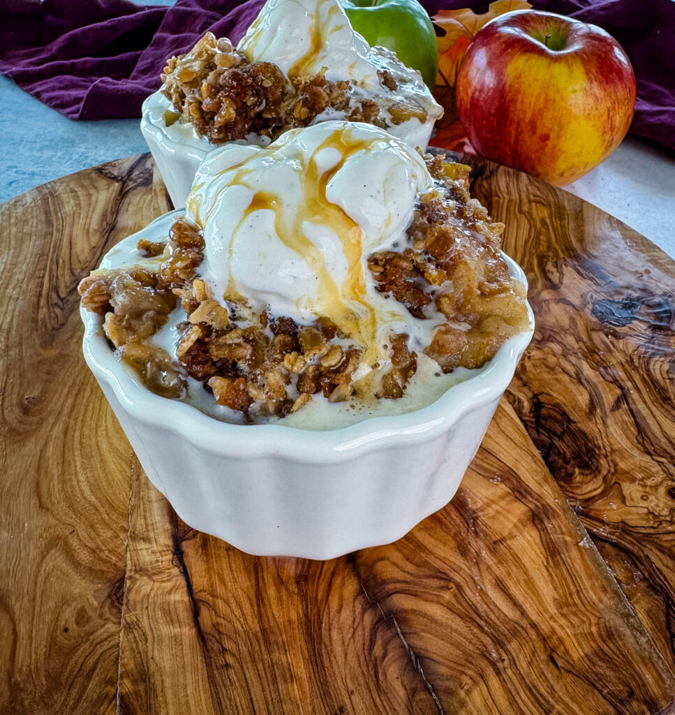 slow cooker Crockpot apple crisp in a white bowl with a scoop of vanilla ice cream and caramel