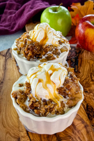 slow cooker Crockpot apple crisp in a white bowl with a scoop of vanilla ice cream and caramel