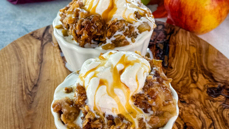 slow cooker Crockpot apple crisp in a white bowl with a scoop of vanilla ice cream and caramel