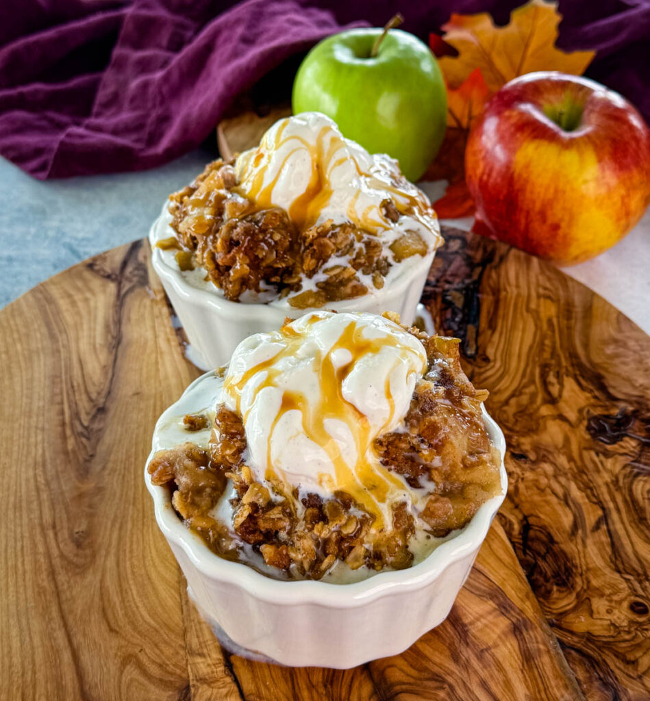 slow cooker Crockpot apple crisp in a white bowl with a scoop of vanilla ice cream and caramel