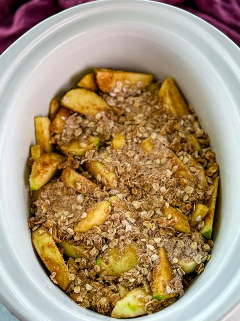 sliced apples with cinnamon and sugar with a crumble topping in a white Crockpot slow cooker