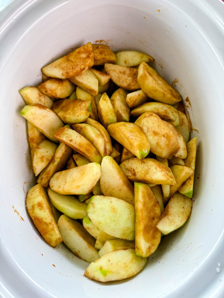 sliced apples with cinnamon and sugar in a white Crockpot slow cooker