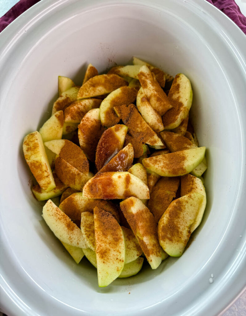 sliced apples with cinnamon and sugar in a white Crockpot slow cooker