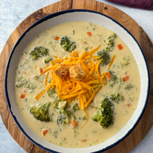 broccoli cheddar soup in a white bowl with grated cheddar cheese and croutons