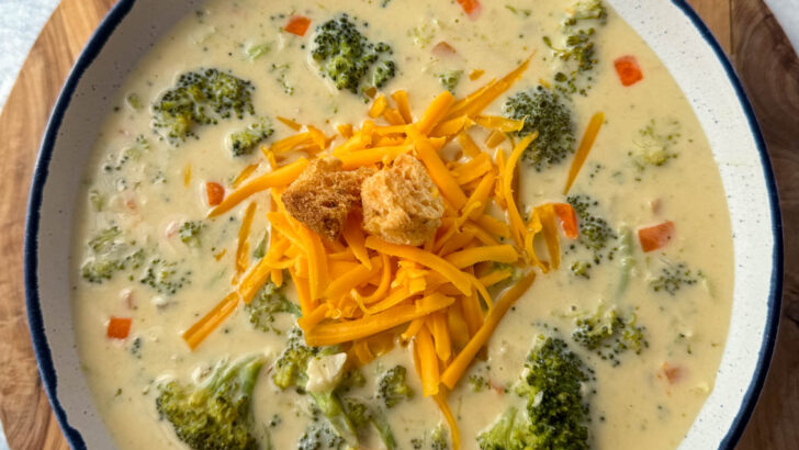 broccoli cheddar soup in a white bowl with grated cheddar cheese and croutons