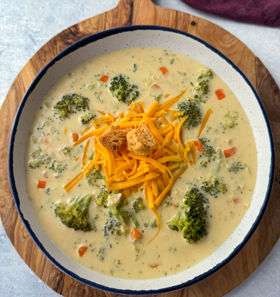 broccoli cheddar soup in a white bowl with grated cheddar cheese and croutons