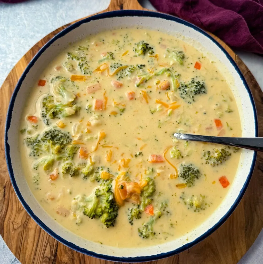 broccoli cheddar soup in a white bowl with a spoon and grated cheddar cheese