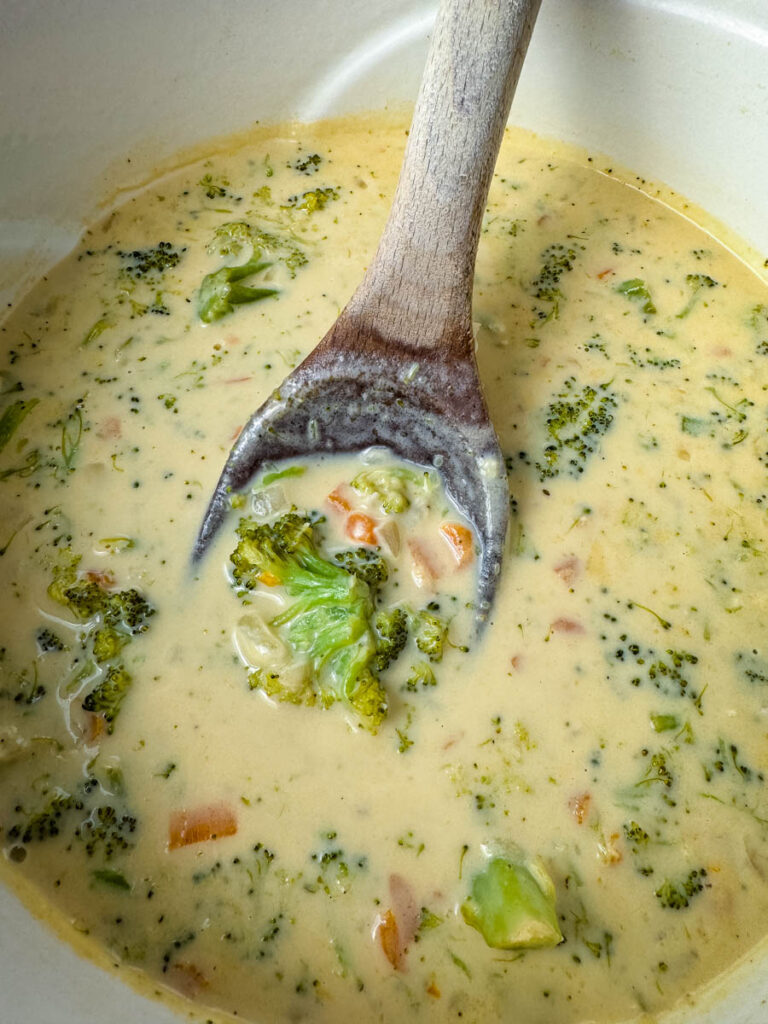 broccoli cheddar soup in a Dutch oven with a wooden spoon