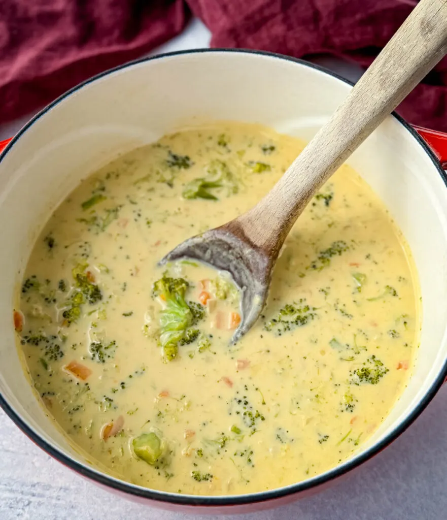 broccoli cheddar soup in a Dutch oven with a wooden spoon