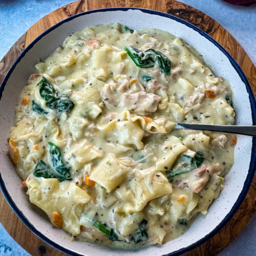 white lasagna soup in a bowl with carrots, celery, and spinach