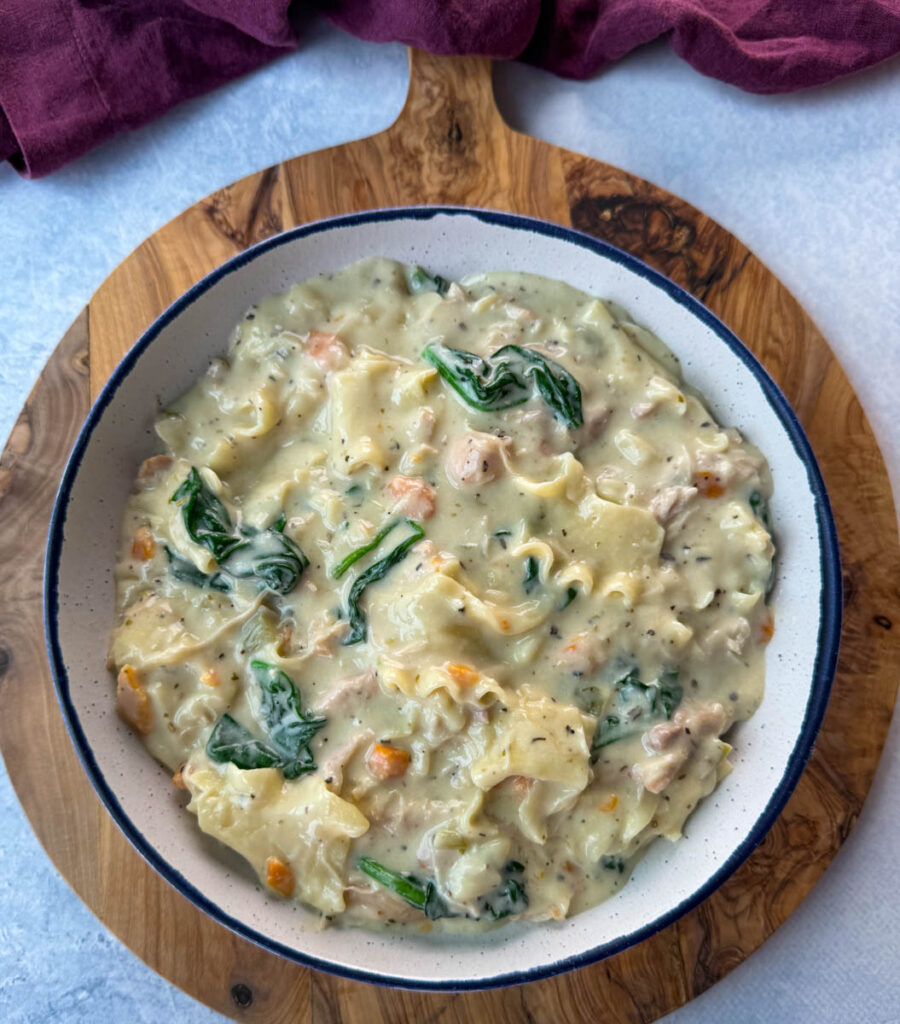 white lasagna soup in a bowl with carrots, celery, and spinach