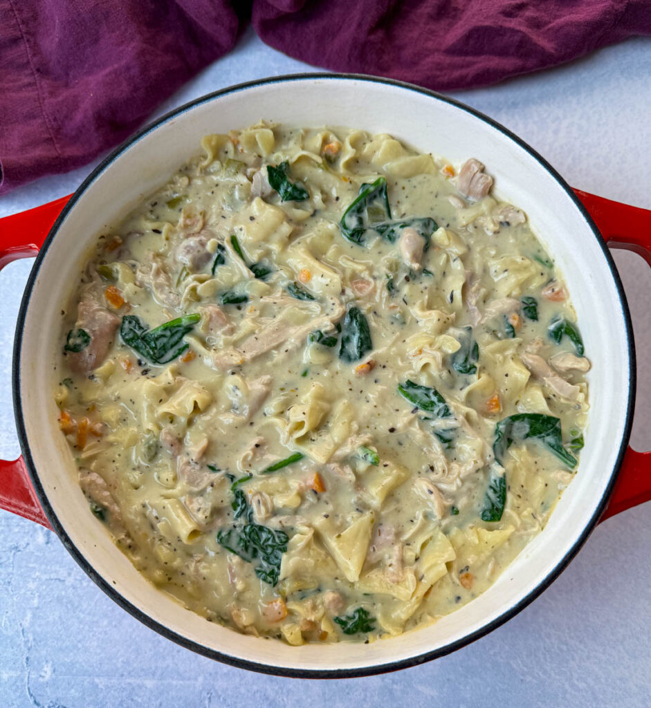 white lasagna soup in a Dutch oven with carrots, celery, and spinach