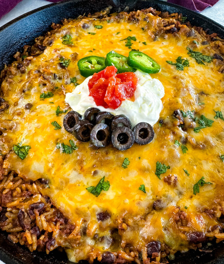 Mexican beef and rice taco skillet dish in a cast iron skillet with sour cream, tomatoes, and black olives