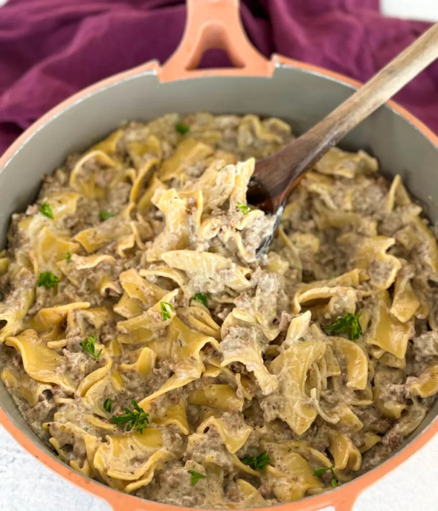 beef and noodles in a skillet with a wooden spoon