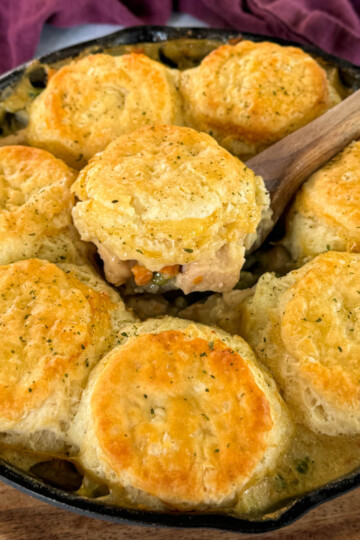 a wooden spoonful of chicken pot pie with biscuits in a cast iron skillet