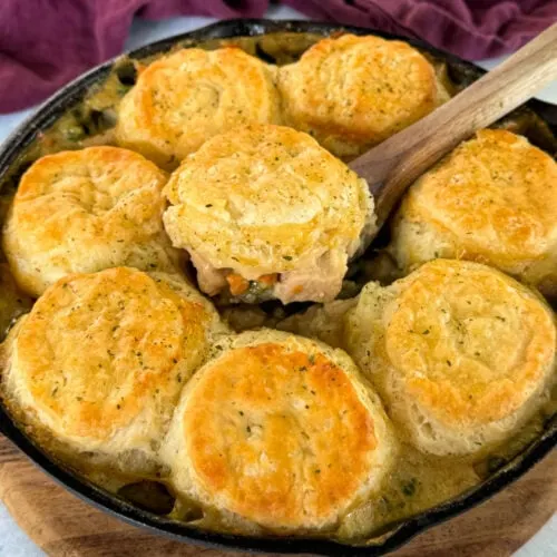 a wooden spoonful of chicken pot pie with biscuits in a cast iron skillet