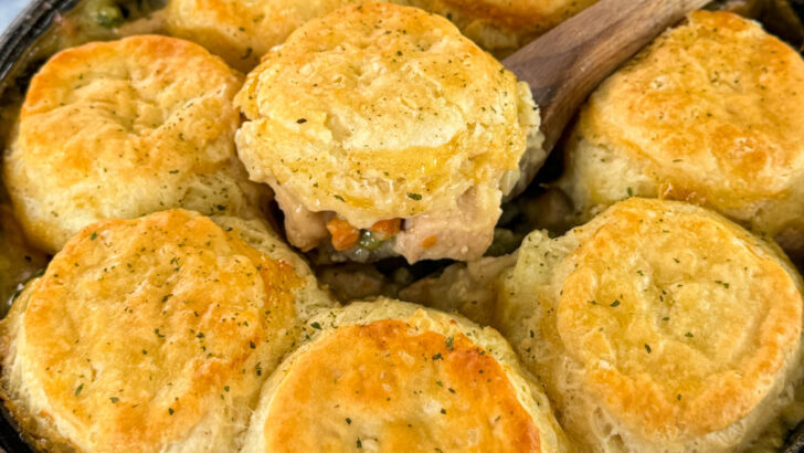 a wooden spoonful of chicken pot pie with biscuits in a cast iron skillet