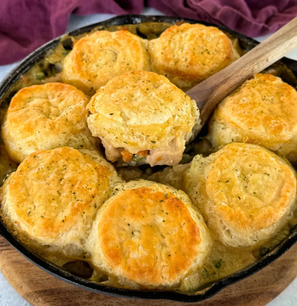 a wooden spoonful of chicken pot pie with biscuits in a cast iron skillet