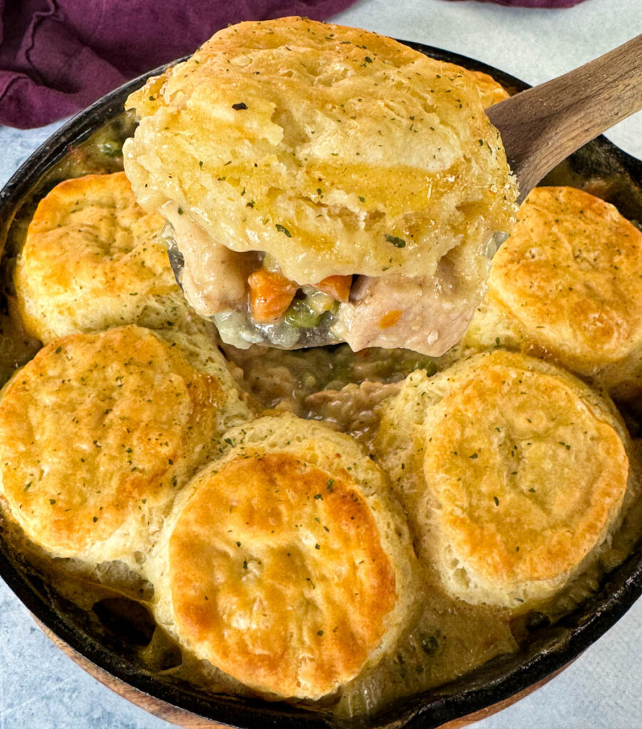 a wooden spoonful of chicken pot pie with biscuits in a cast iron skillet