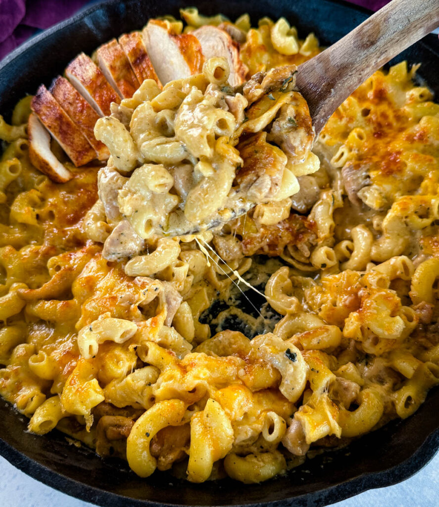 chicken mac and cheese in a cast iron skillet with a wooden spoon