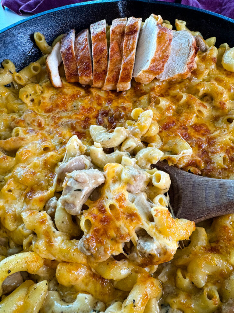 chicken mac and cheese in a cast iron skillet with a wooden spoon