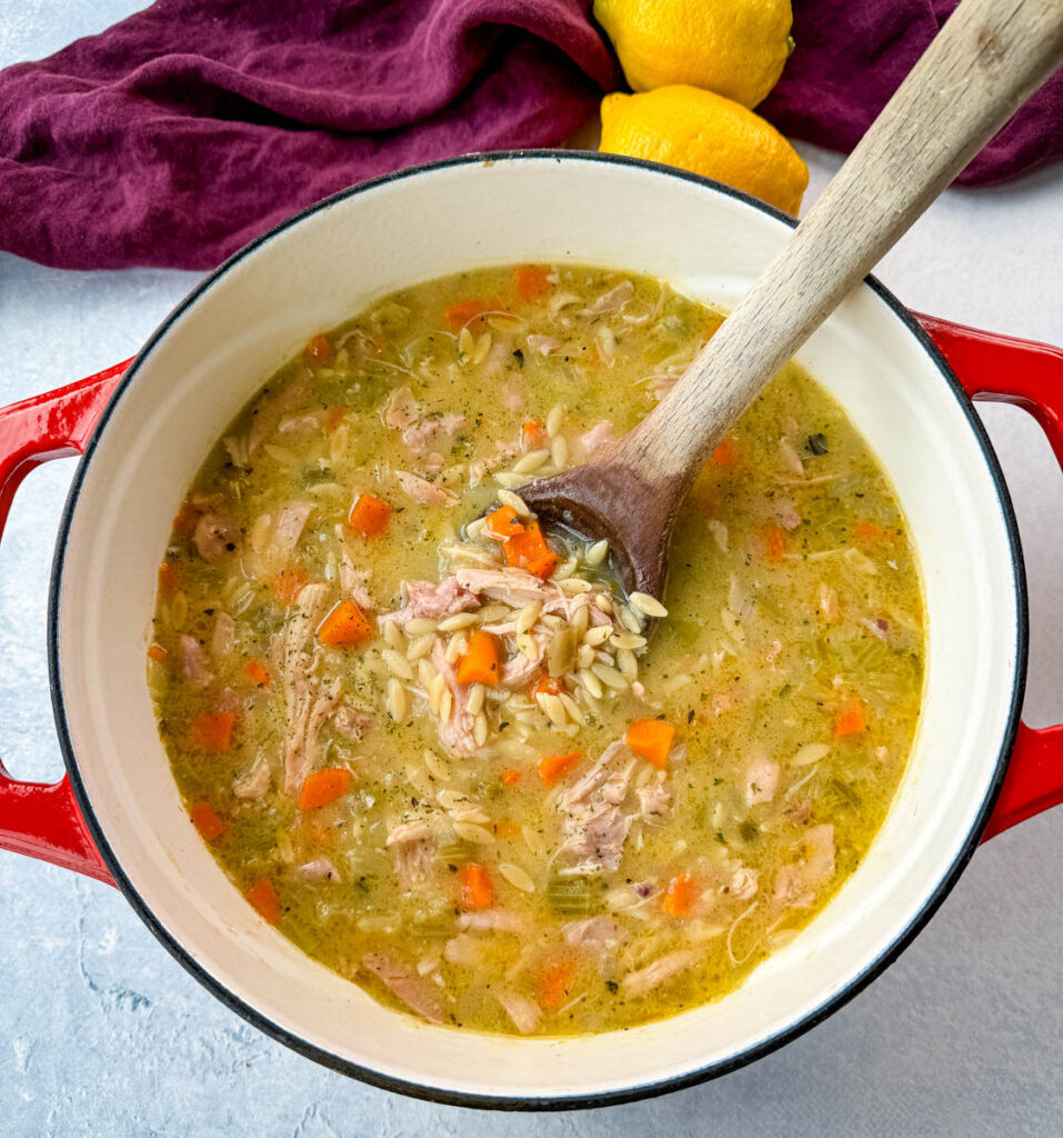 chicken orzo soup with carrots, celery, and a wooden spoon in a red Dutch oven