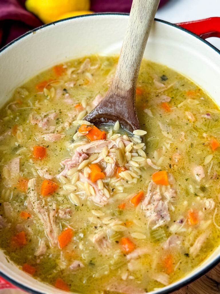 chicken orzo soup with carrots, celery, and a wooden spoon in a red Dutch oven